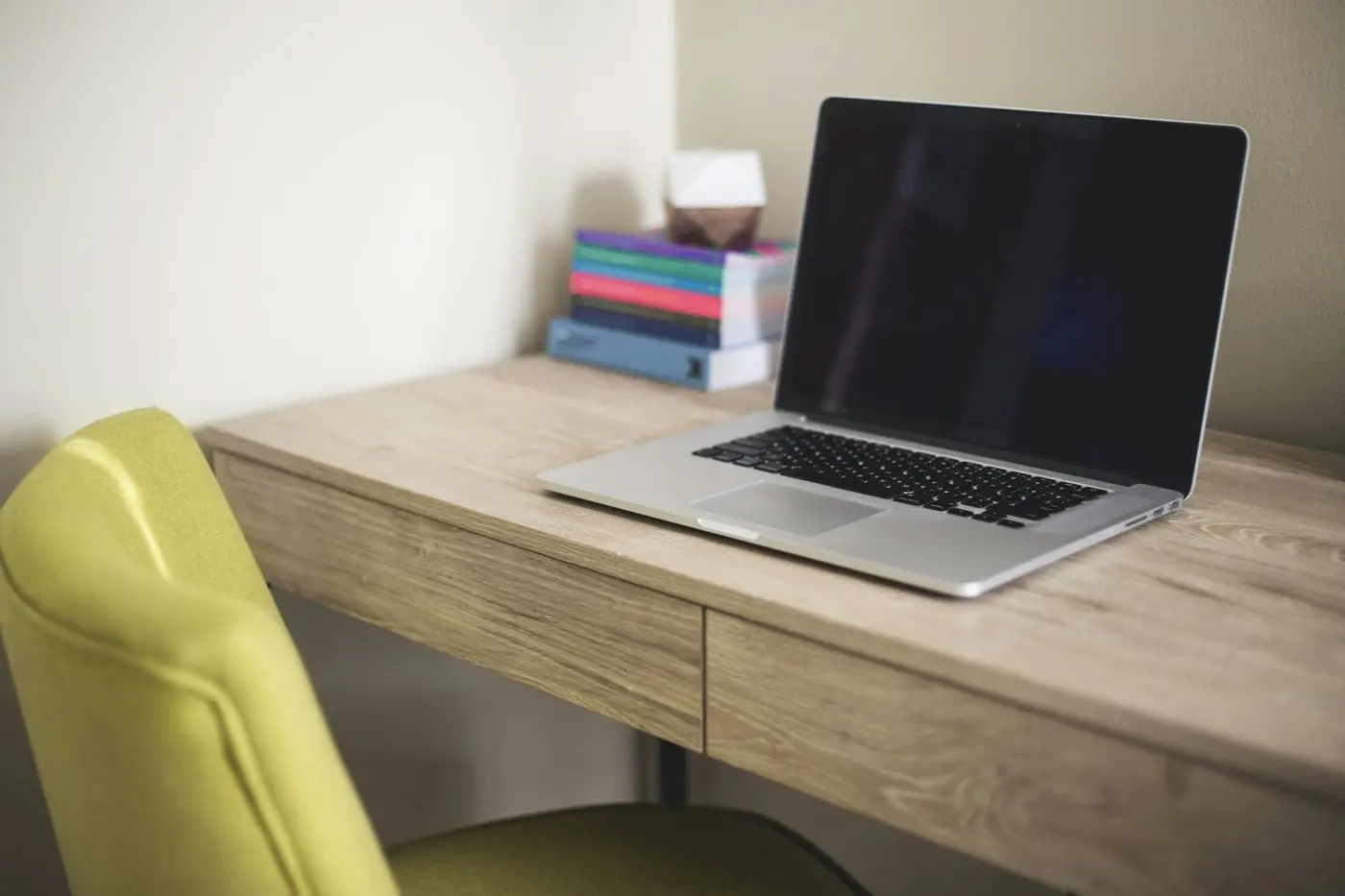 Open laptop on a light wooden desk beside books